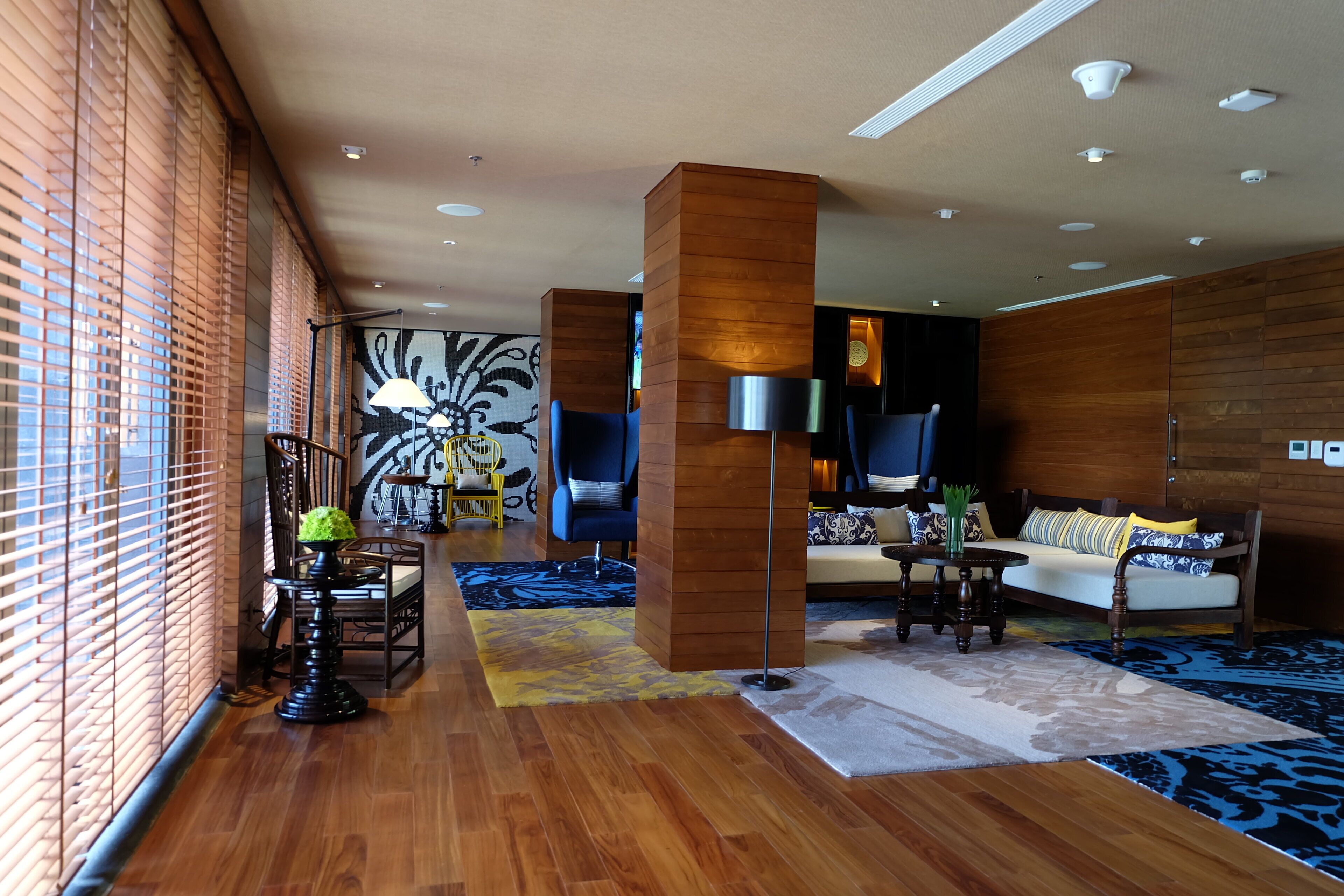 Um hall de hotel moderno com piso de madeira, um sofá, cadeiras e um tapete estampado.