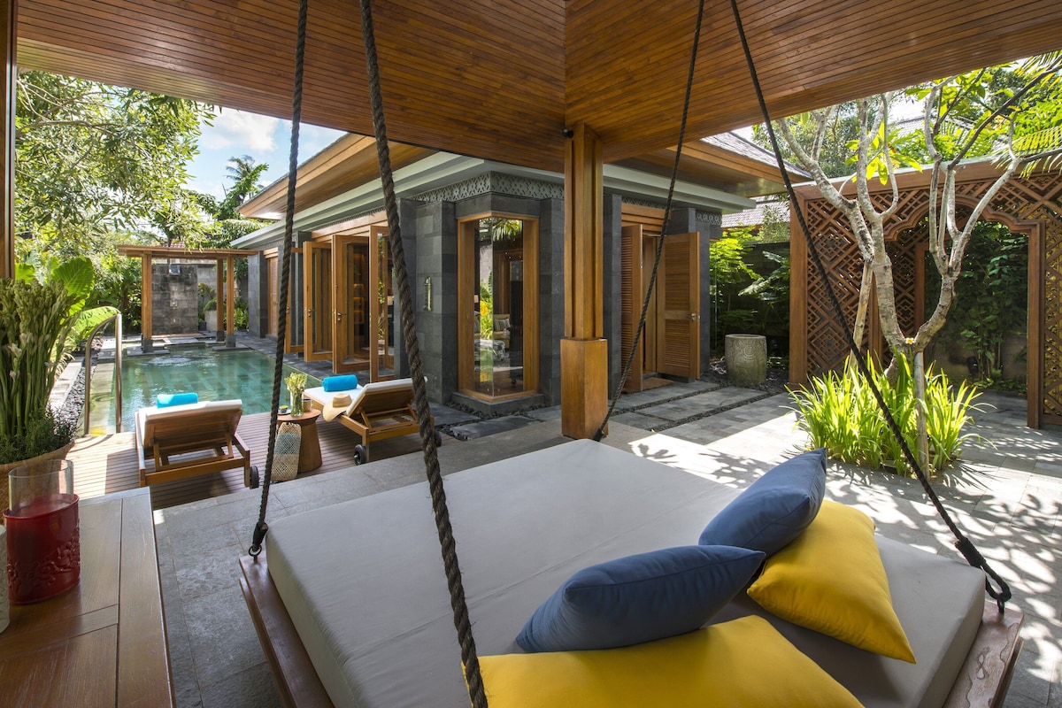 A modern outdoor lounge area with a pool, wooden furniture, and tropical plants.