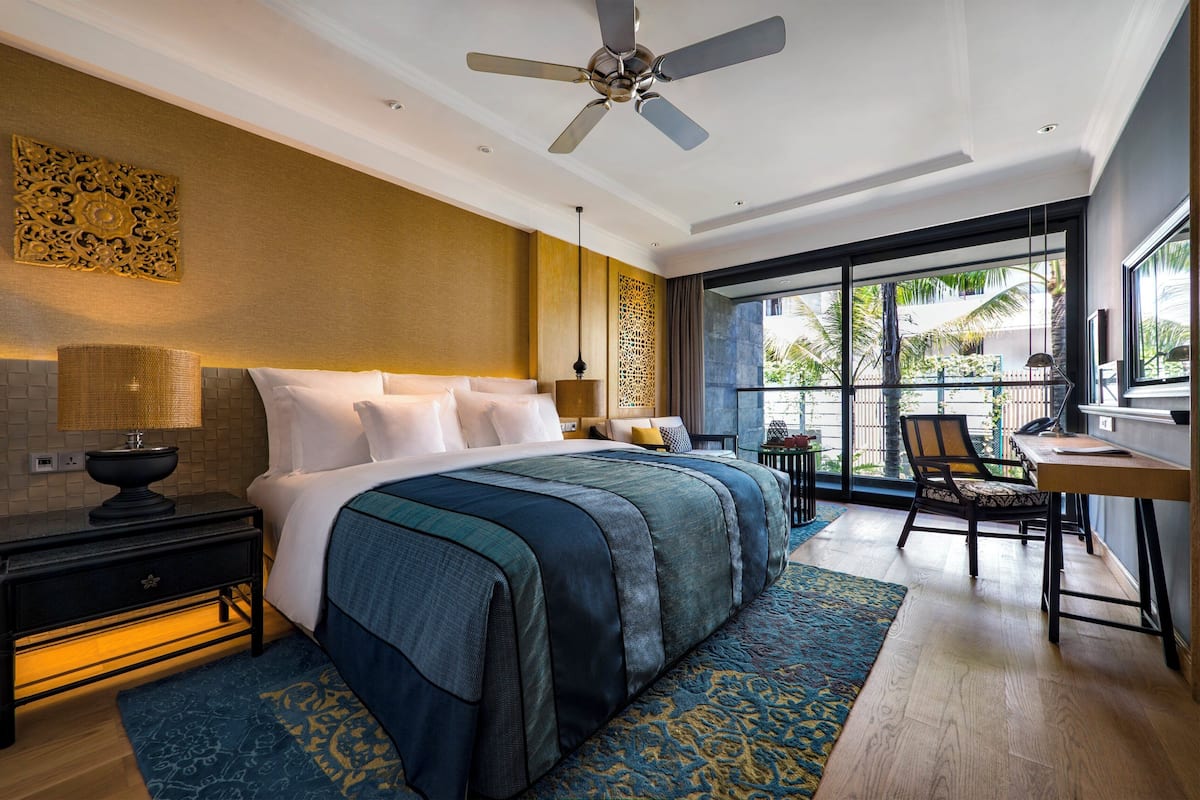 Ein Hotelzimmer mit Bett, Schreibtisch, Stuhl, Deckenventilator und einem großen Fenster.