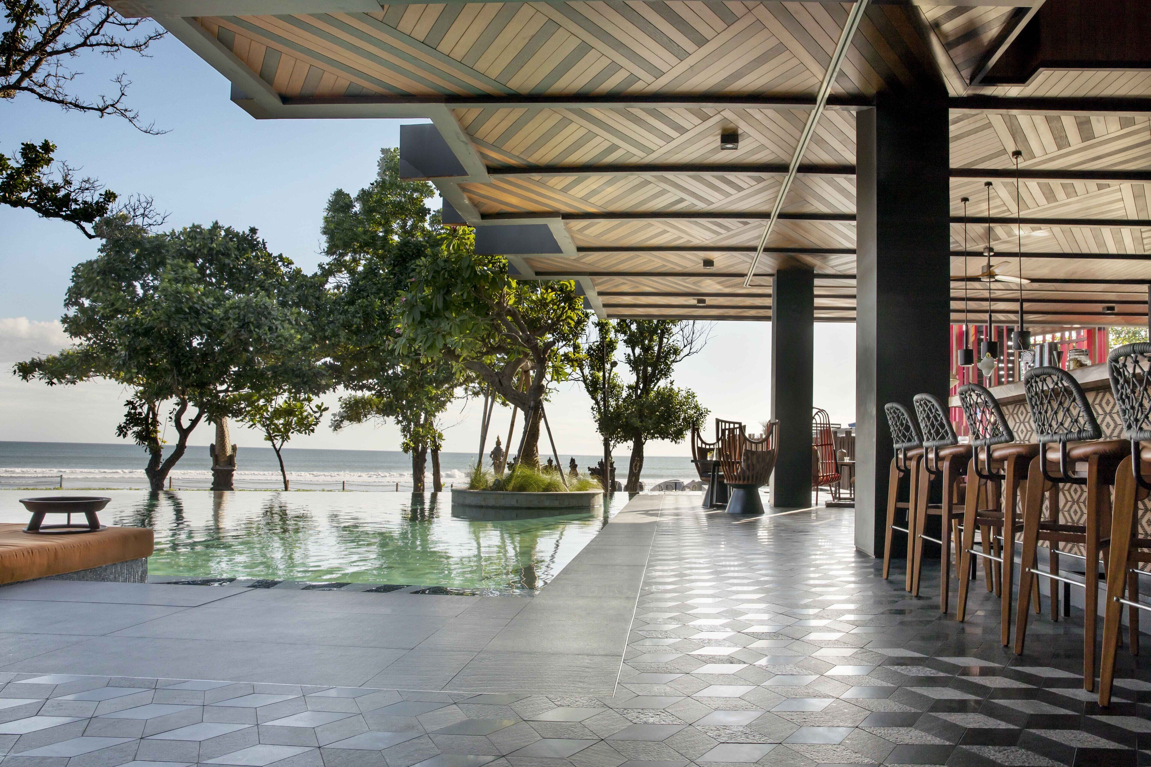A covered outdoor area with a pool, seating, and a view of the sea.