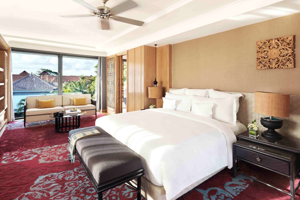 Ein geräumiges Hotelzimmer mit einem großen Bett, einem Sofa, einer Bank, einem Nachttisch und Blick auf einen Pool und Grünflächen.