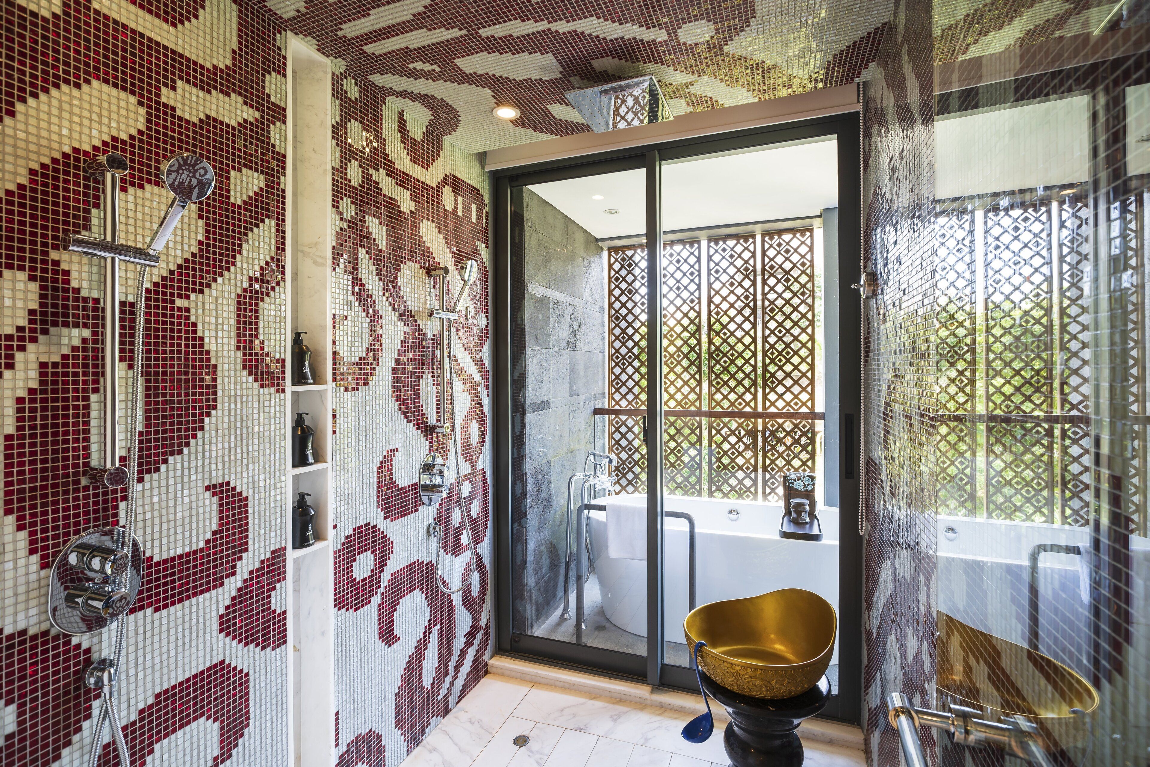 A bathroom with mosaic tile walls, a large gold bowl, and a glass-enclosed shower area.