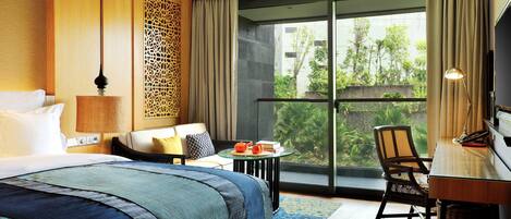 Quarto de hotel com uma cama grande, uma escrivaninha com cadeira, uma mesa com chaleira e vista para o verde lá fora.