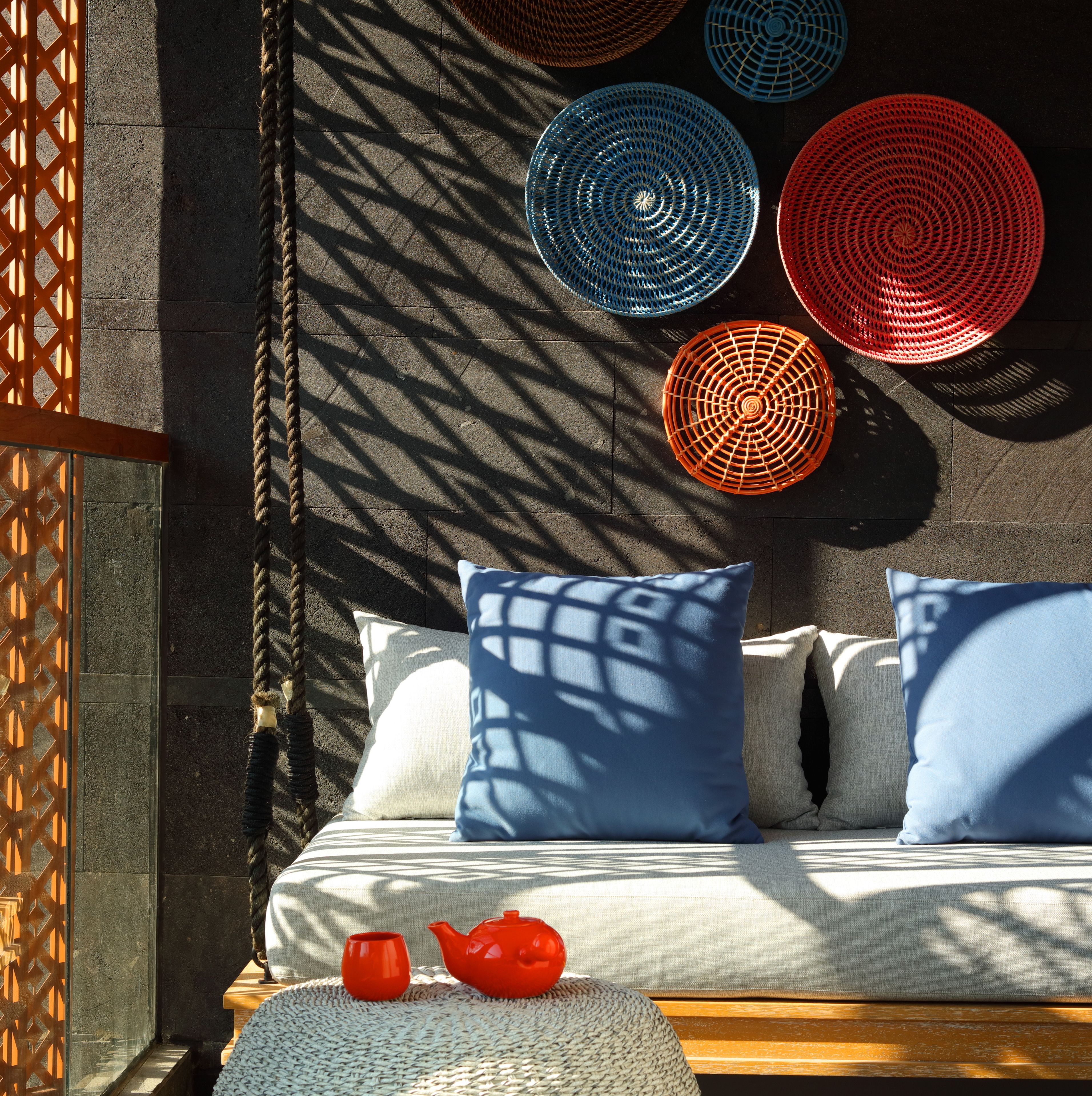 A room with a hanging swing, a woven rug, and a wooden bench with a red teapot and cup.