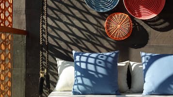 A room with a hanging swing, a woven rug, and a wooden bench with a red teapot and cup.