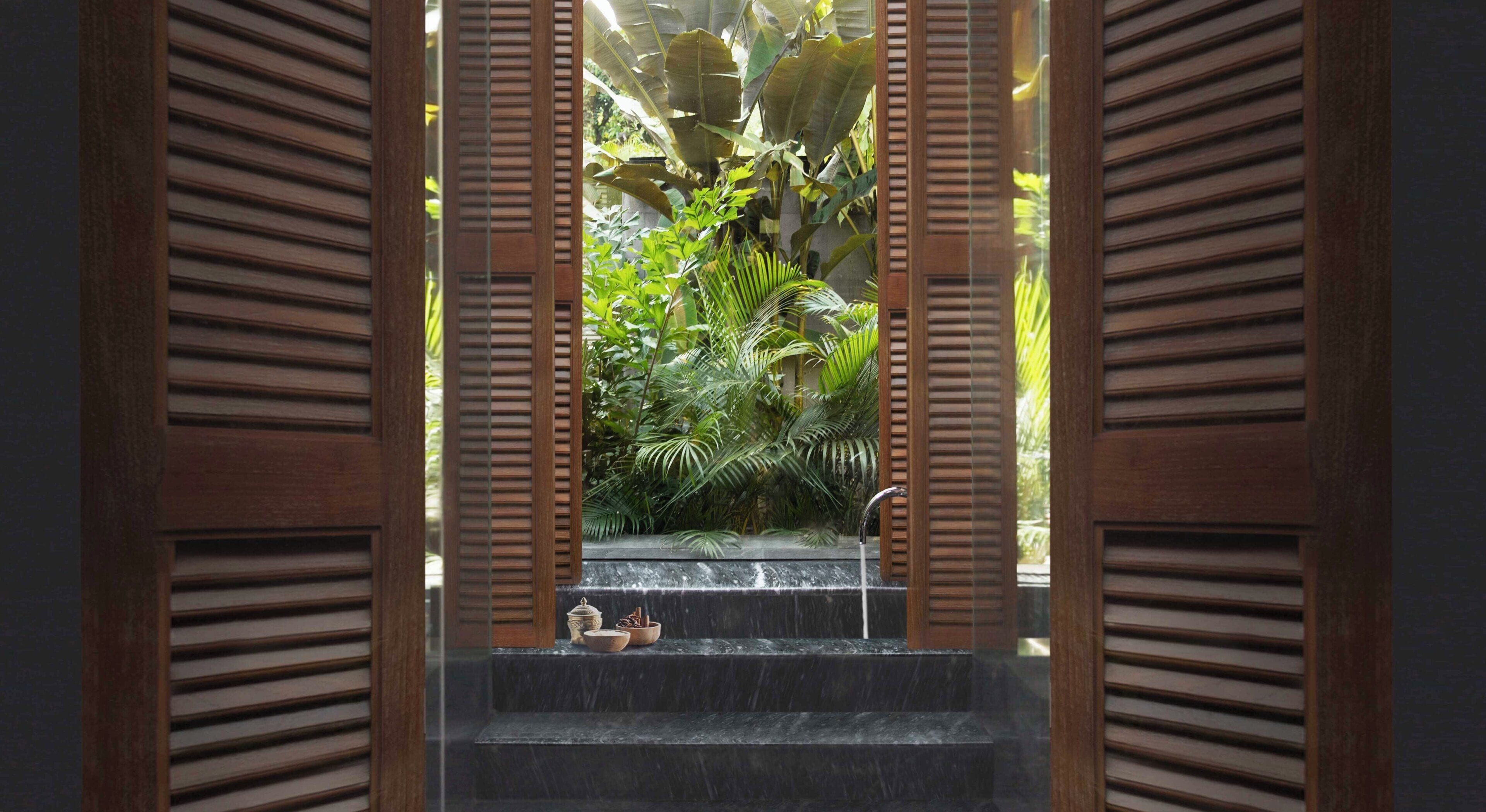 A view through wooden shutters to a water feature with steps and a small table with items.