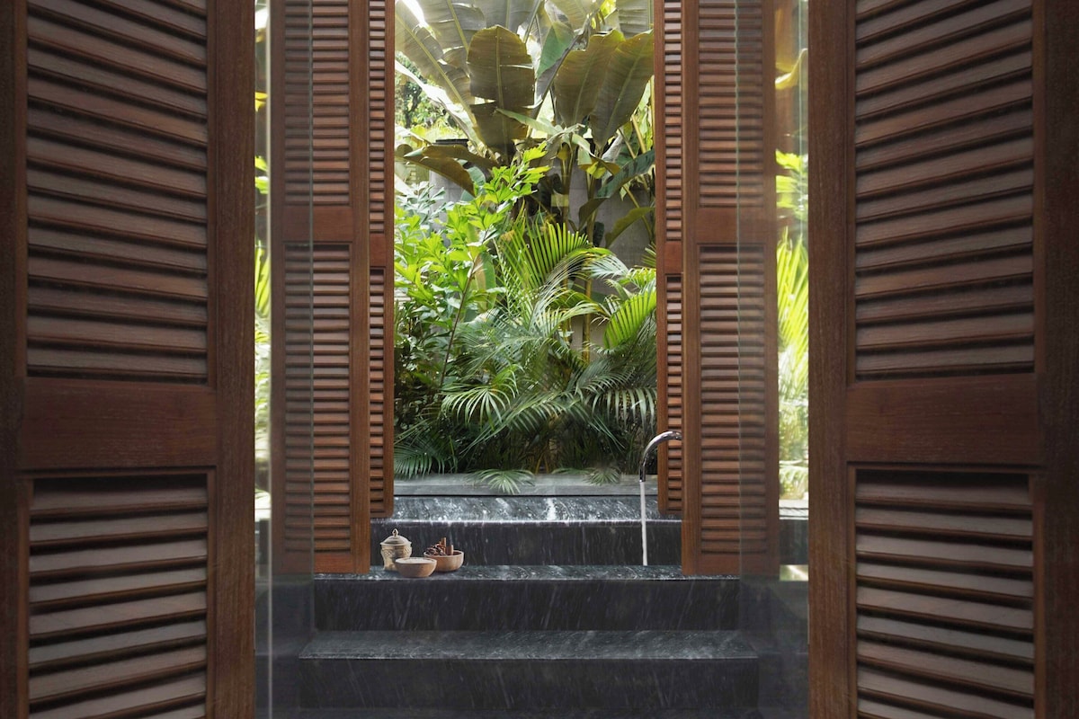 A view through wooden shutters to a water feature with steps and a small table with bowls.
