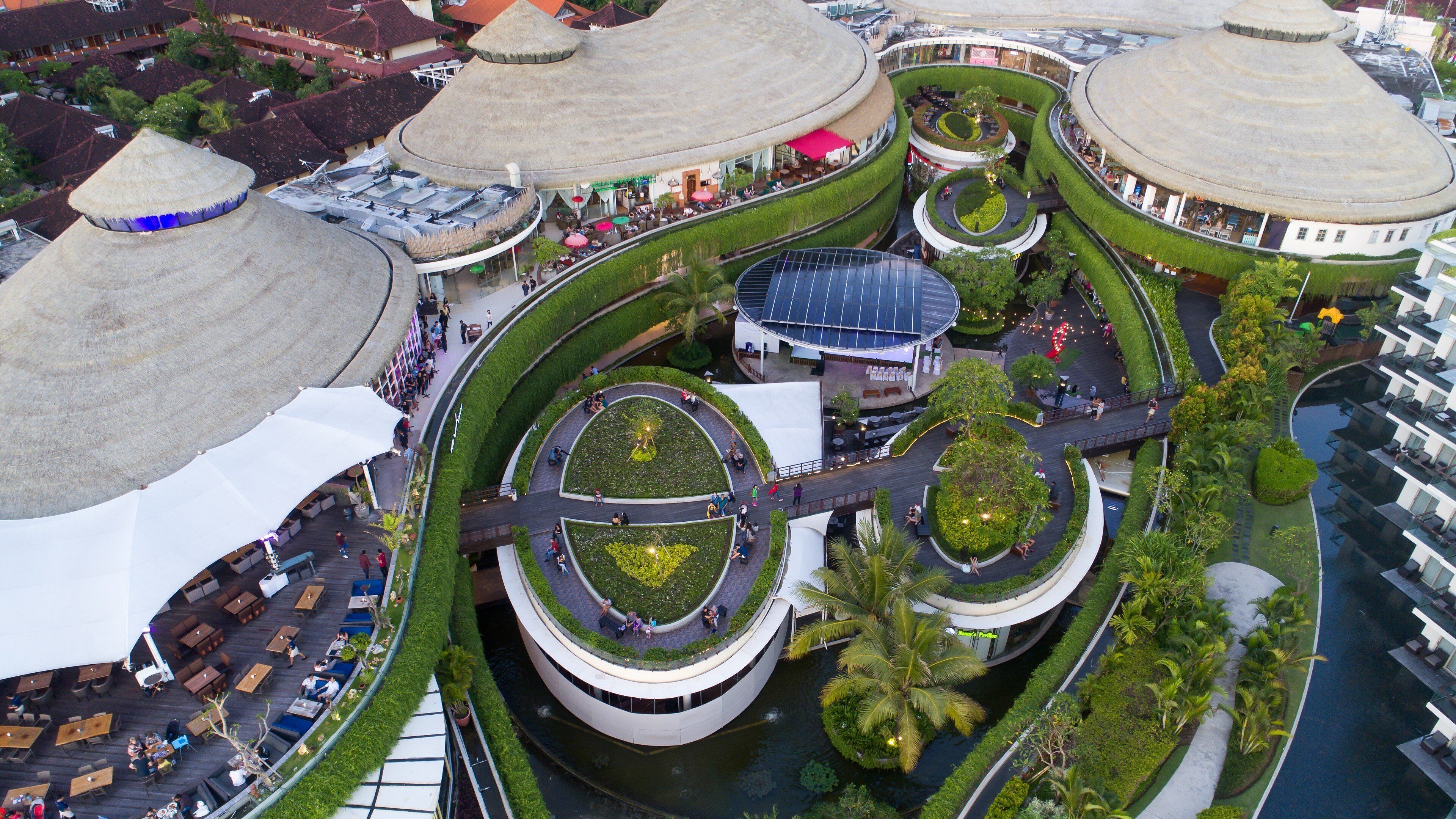 A multi-level hotel with circular and curved architecture, featuring outdoor seating areas and a central water feature.