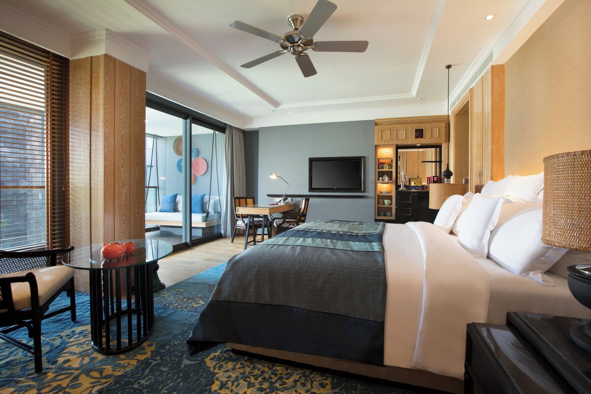 A hotel room with a bed, a desk, a chair, a television, and a ceiling fan.