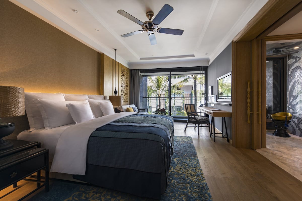 Ein Hotelzimmer mit einem großen Bett, einem Schreibtisch und Blick auf Palmen durch das Fenster.