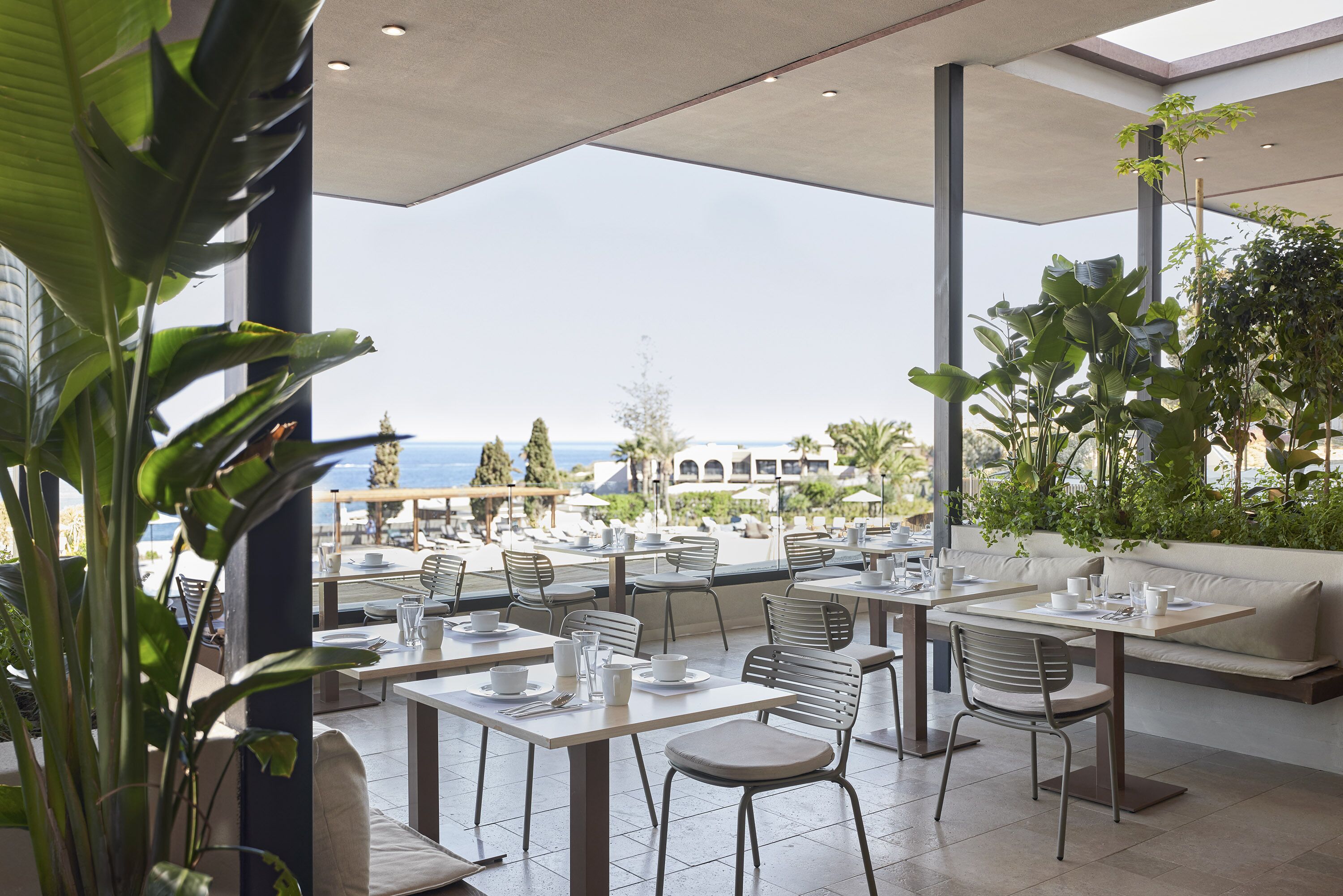 A restaurant with outdoor seating overlooking a scenic view. Tables are set with white tablecloths and chairs.