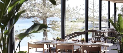 An outdoor dining area with tables set for two, overlooking a body of water.