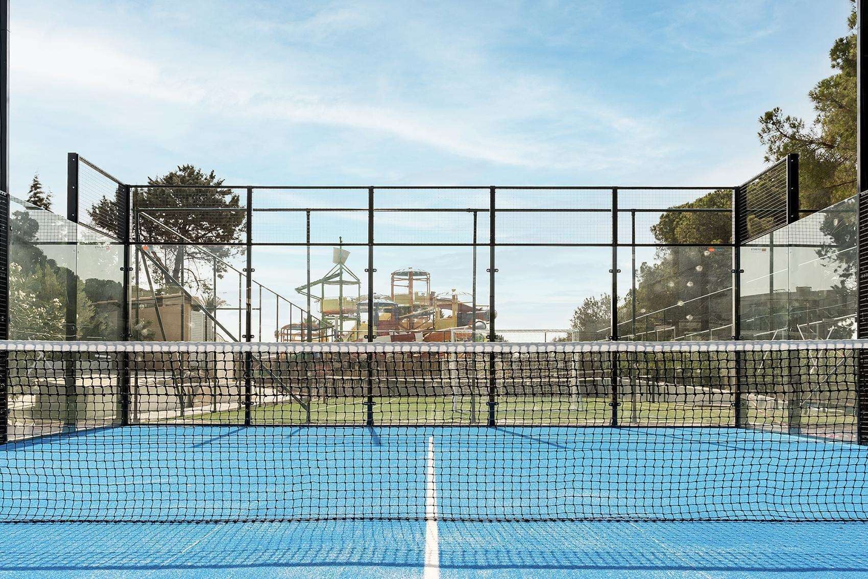An indoor tennis court with a net, surrounded by glass walls and a metal frame structure.