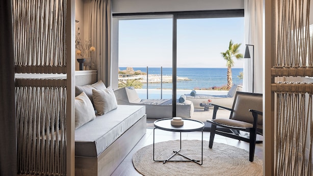 Sala moderna com sofá, poltrona e mesa de centro redonda, com vista para a costa.