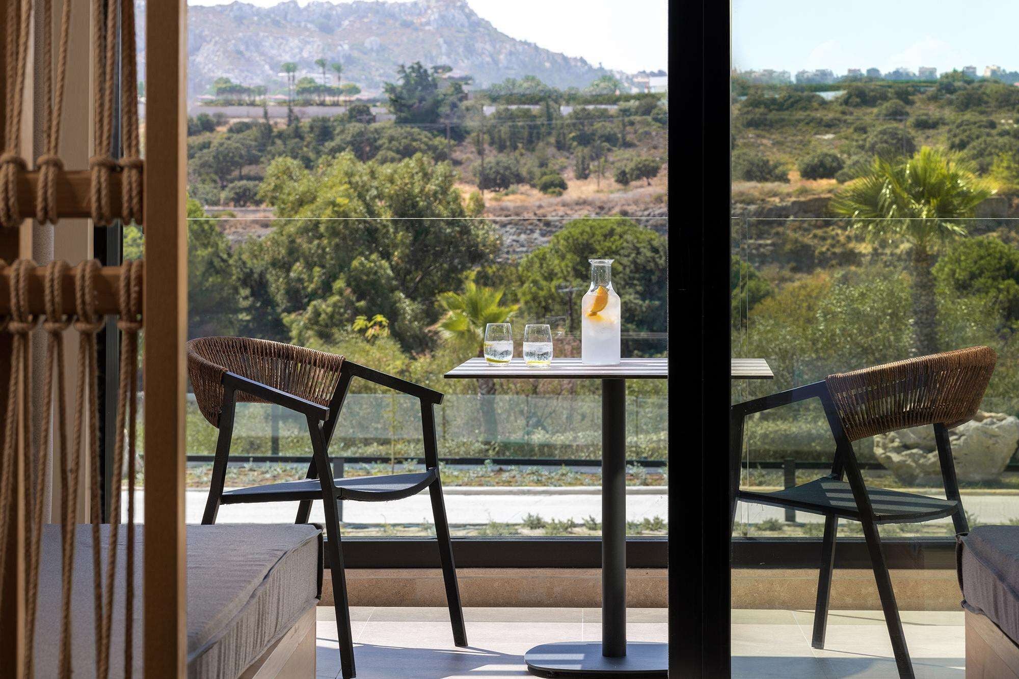 A balcony with two wicker chairs, a table, and a bottle with glasses.