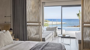 Quarto de hotel com cama, sofá, mesinha e vista para o oceano.