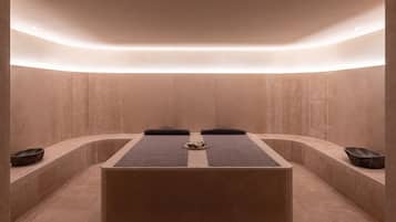 Ein Spa-Raum mit einem zentral platzierten Massagetisch, zwei seitlichen Bänken und einer kleinen Ablage mit Gegenständen auf dem Tisch.