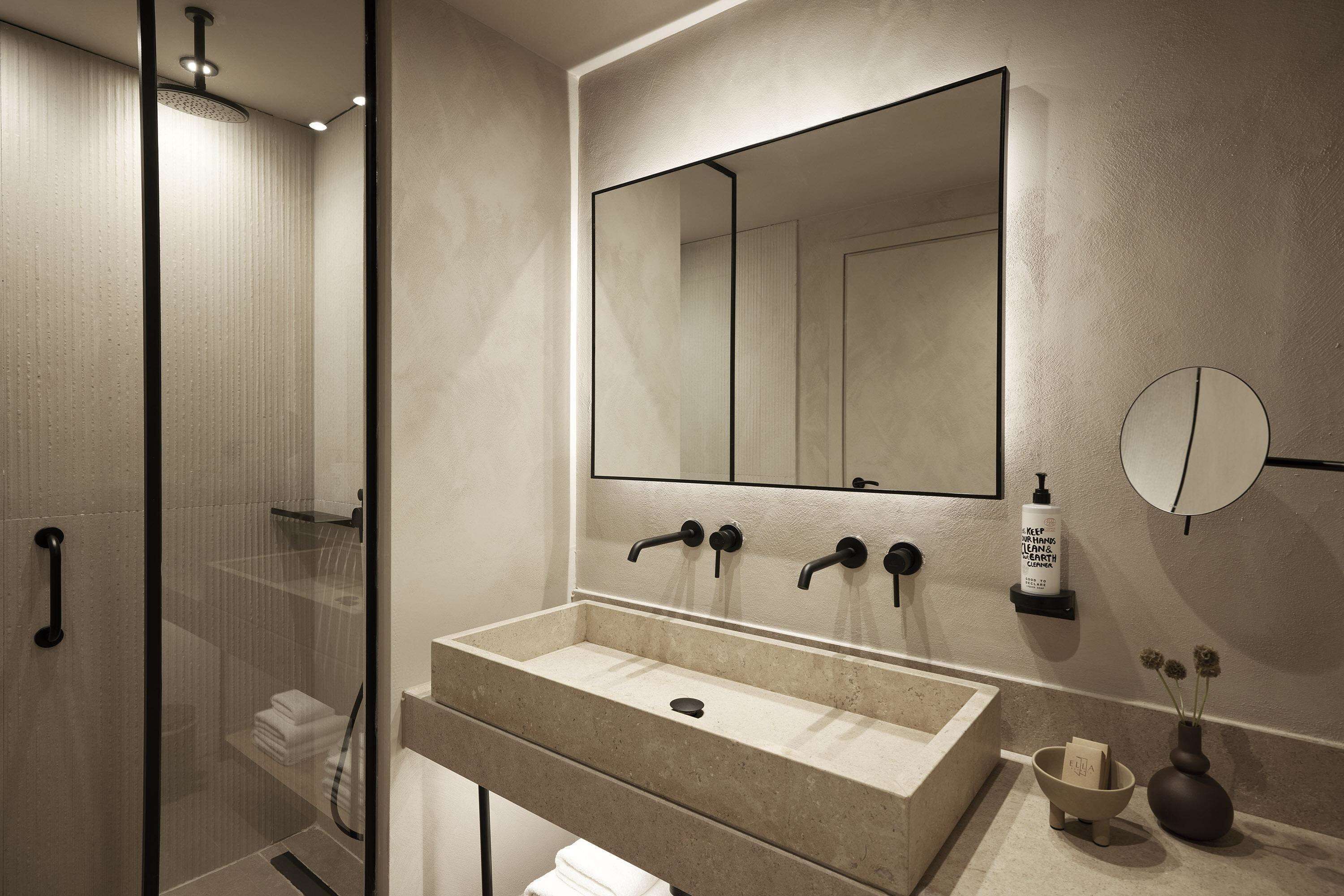 A modern bathroom with a large mirror, a beige sink, and a glass-enclosed shower.