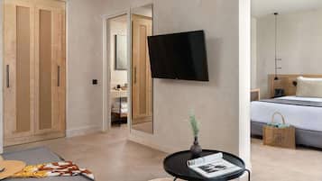 A modern hotel room with a large wardrobe, a flat-screen TV mounted on the wall, a small round table with a magazine, and a bed with a grey headboard.