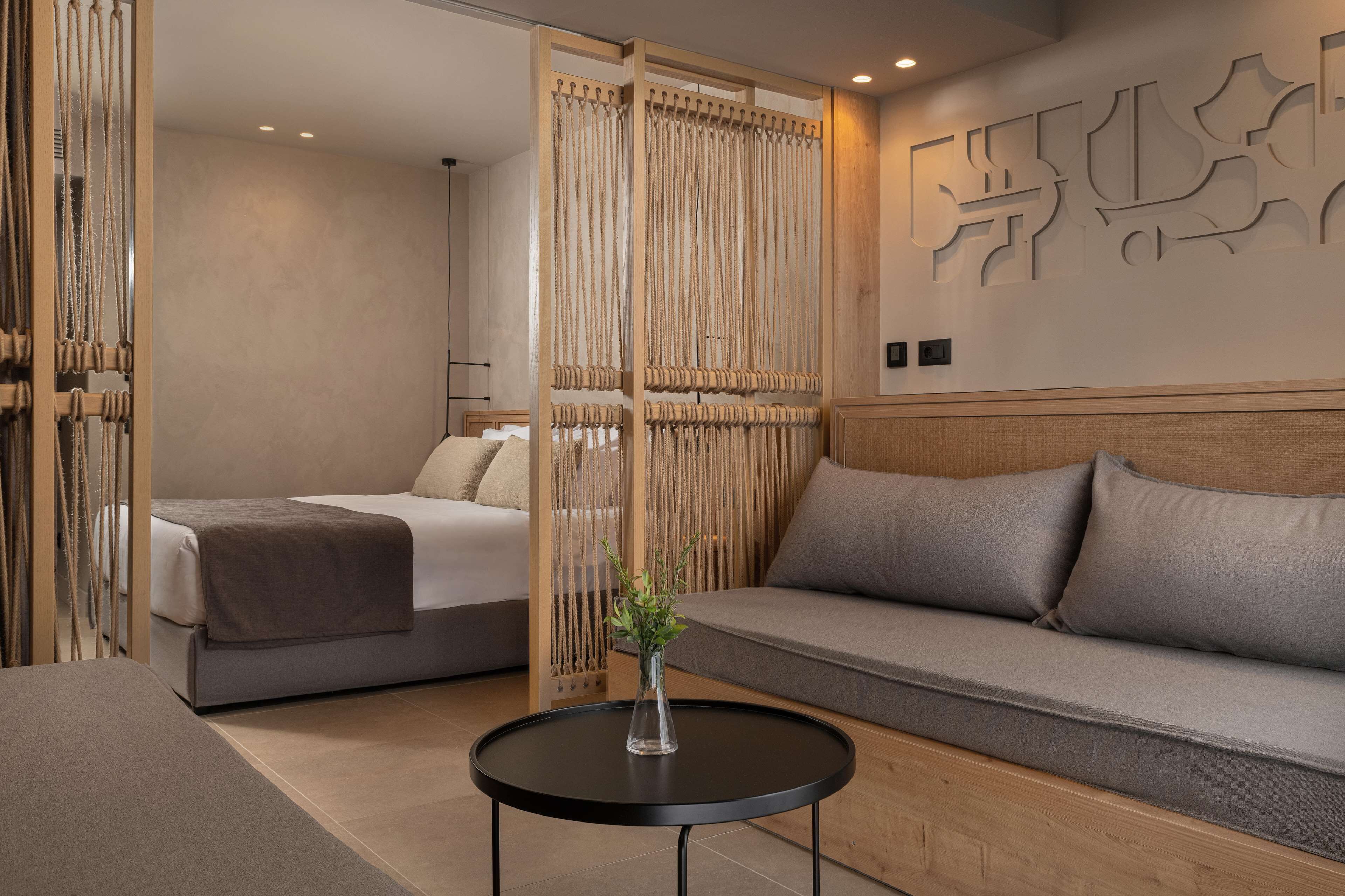 A modern hotel room with a bed, a sofa, a small table with a vase, and a decorative wall piece.