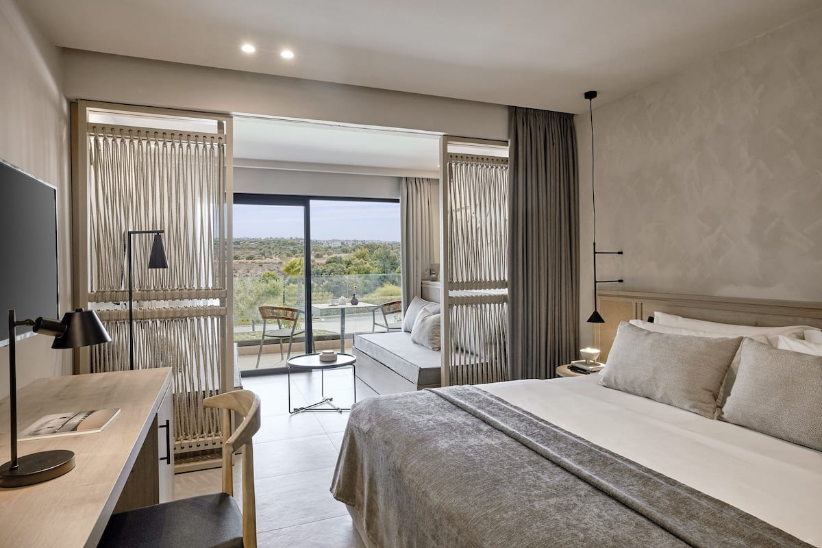 Une chambre d’hôtel moderne dotée d’un grand lit, d’un bureau et d’un balcon offrant une vue sur le paysage.