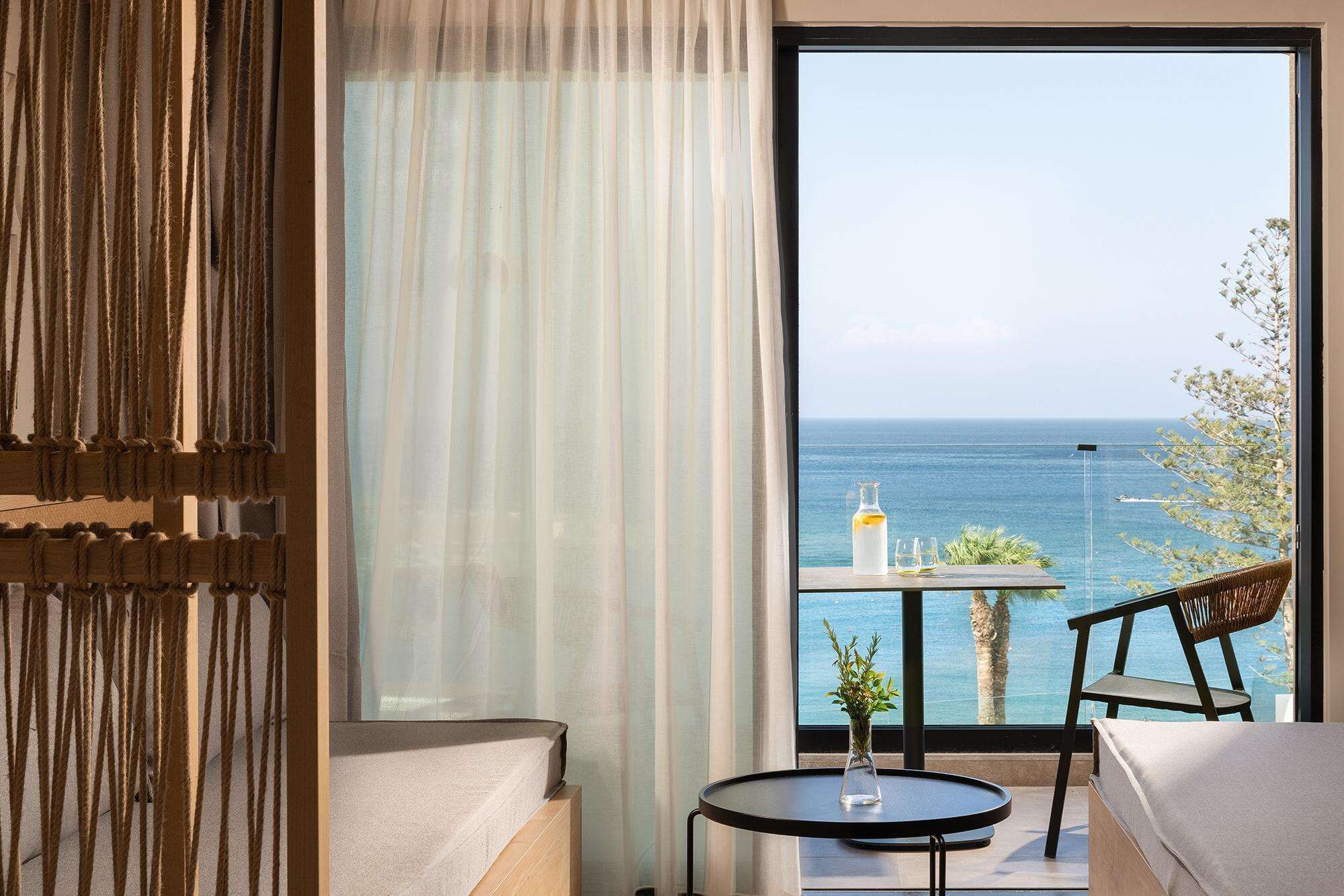 A room with a large window overlooking the sea, a small round table with a vase, and a chair.