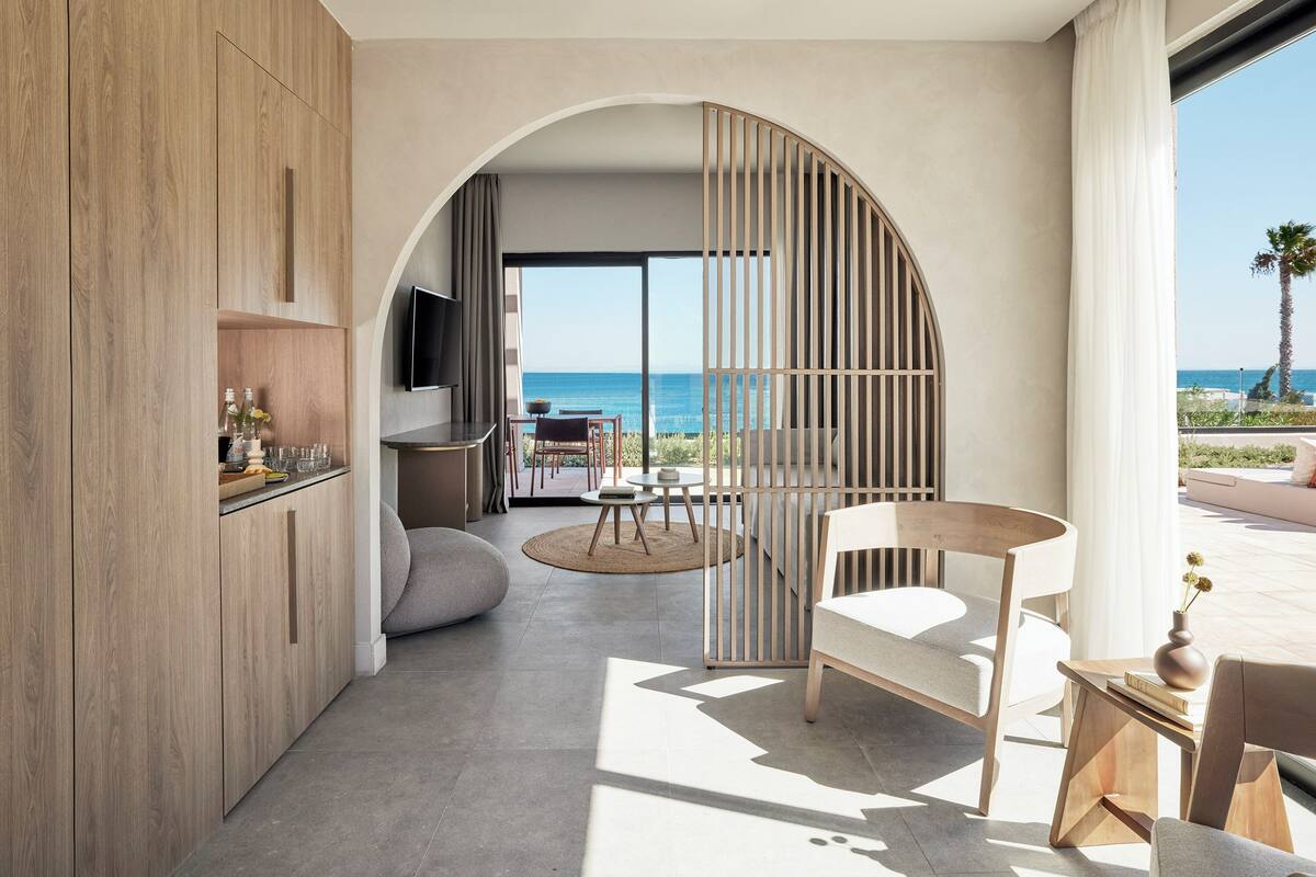 Un intérieur moderne avec un meuble en bois, une table ronde et une chaise, donnant sur un balcon avec vue sur l’océan.
