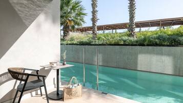 A modern outdoor seating area with a pool, a concrete wall, and palm trees in the background.