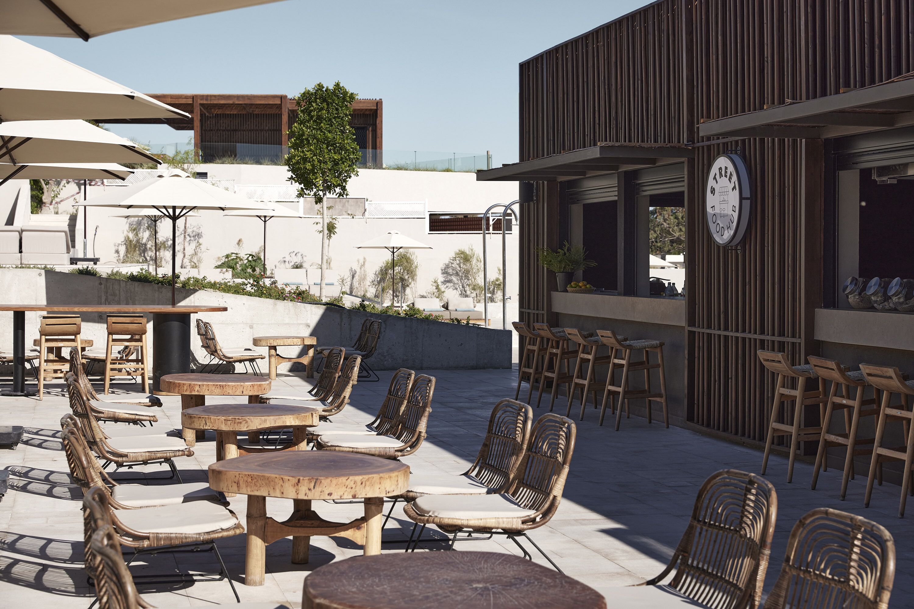 Un espace extérieur aménagé avec des chaises en osier et des tables rondes, un bâtiment en bois avec une enseigne, et un ciel dégagé.