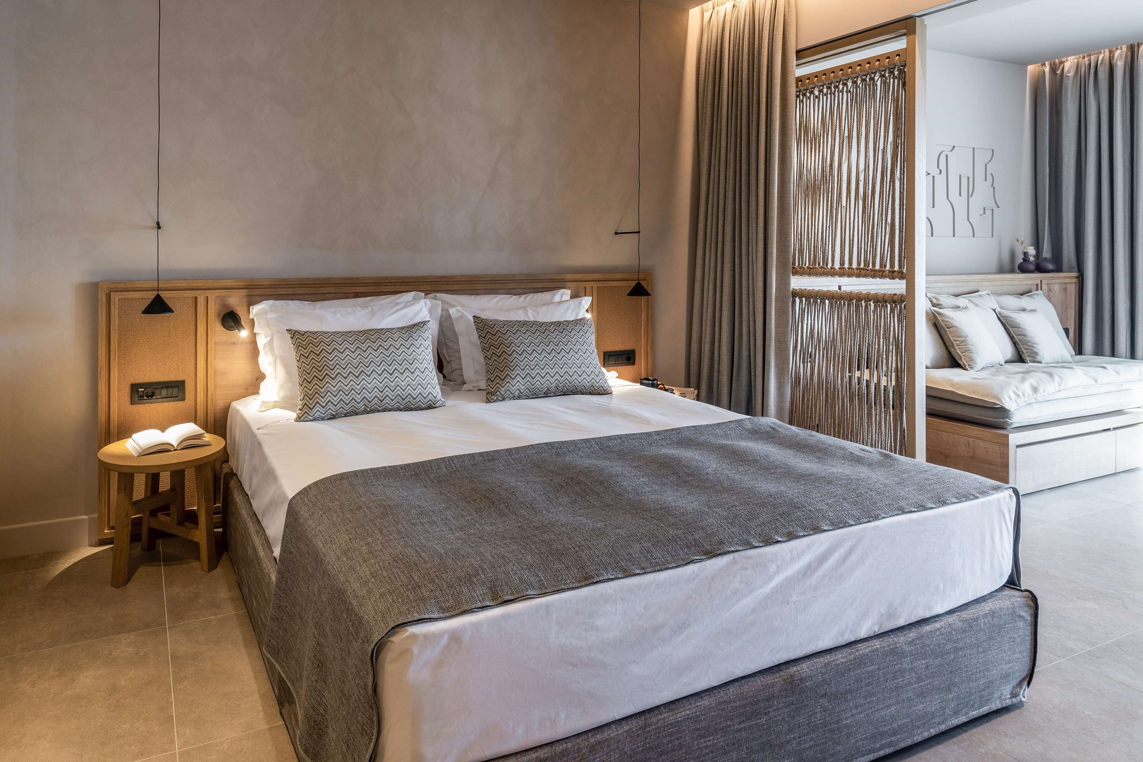 Une chambre d’hôtel moderne avec un grand lit, une table de chevet avec un livre et un miroir agrémenté de rideaux.