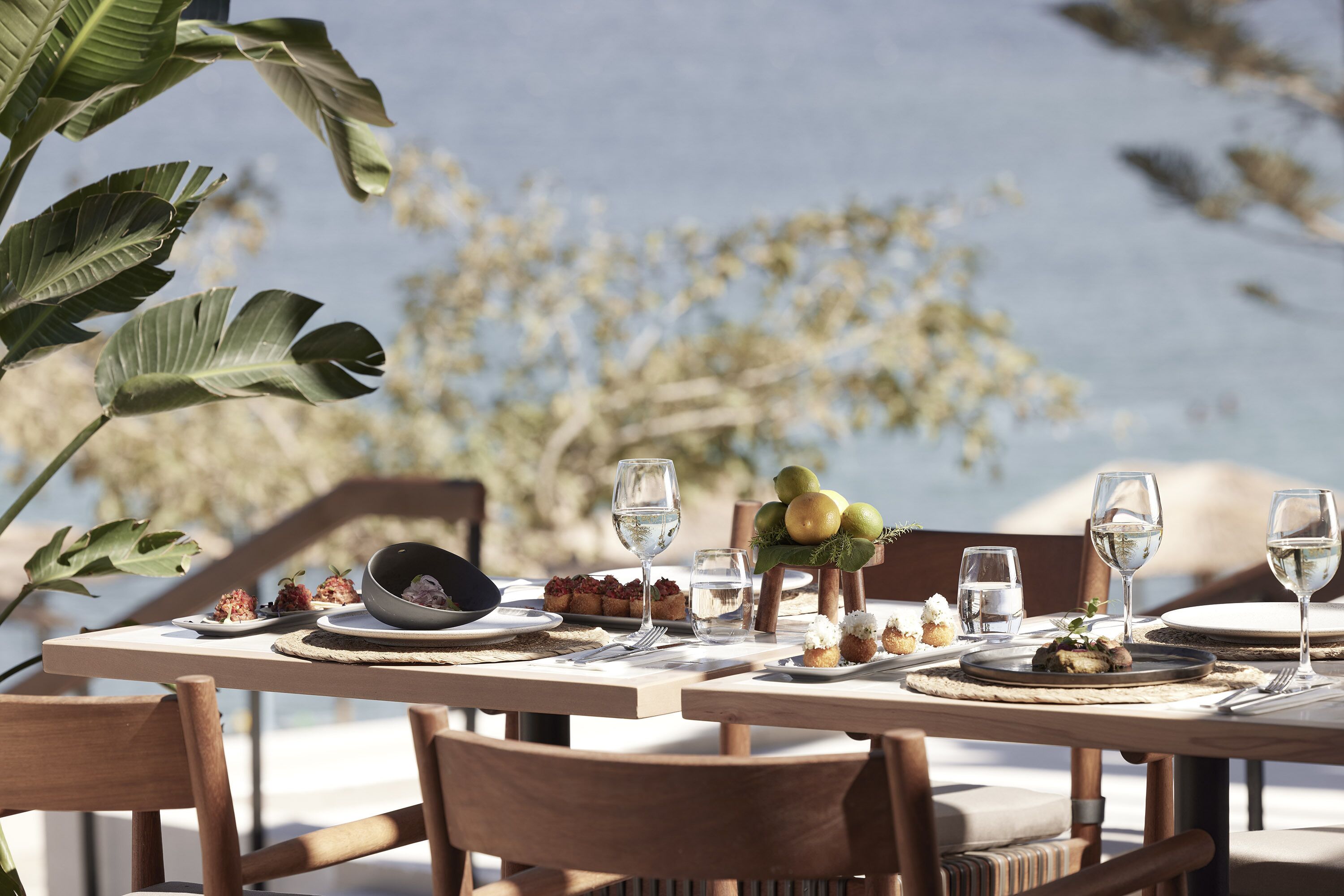 A table set for a meal with plates, glasses, and a bowl of food, surrounded by chairs.
