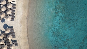 Vista aérea de uma praia com fileiras de guarda-sóis e um mar azul cristalino.