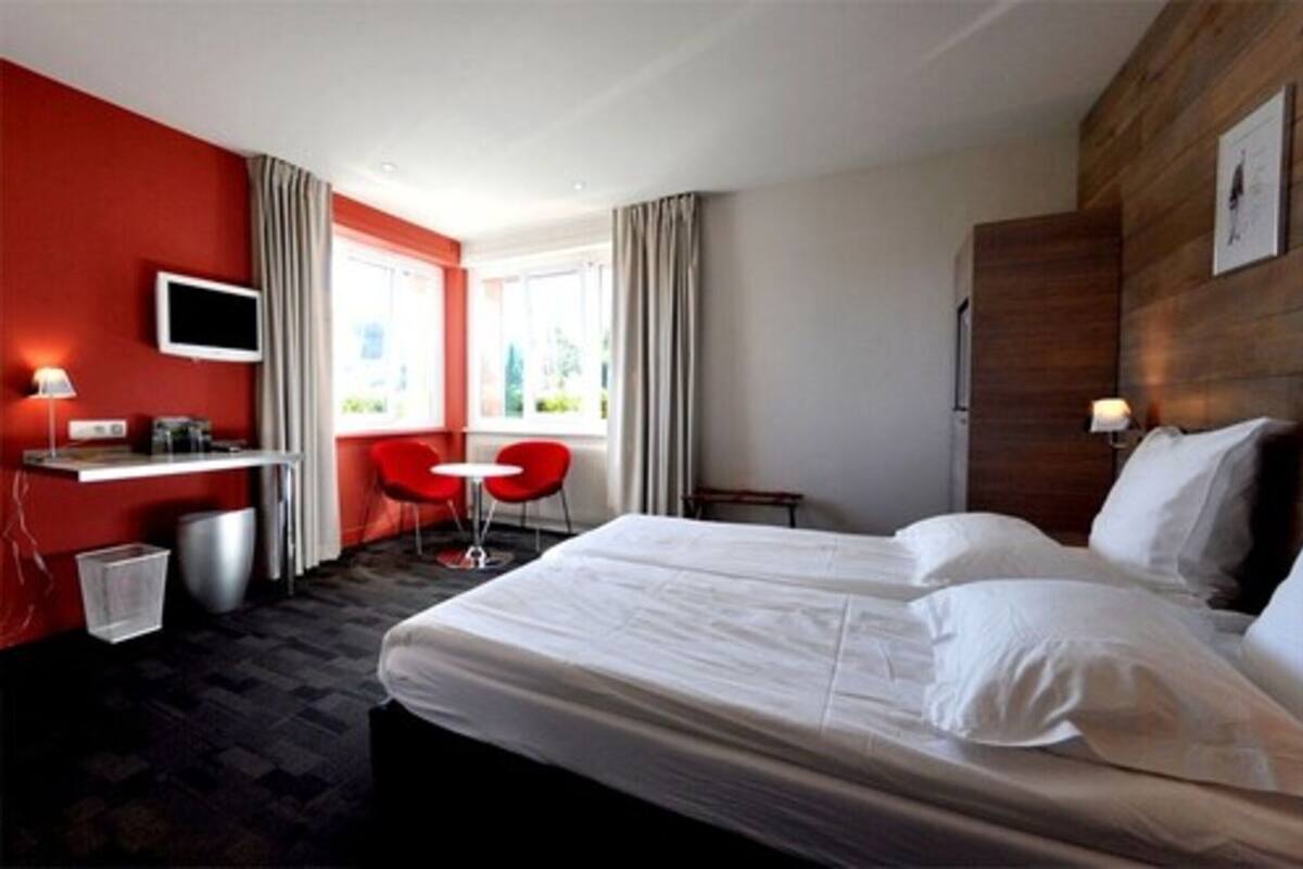 A hotel room with a large bed, a desk with a chair, a TV, and a window with curtains.