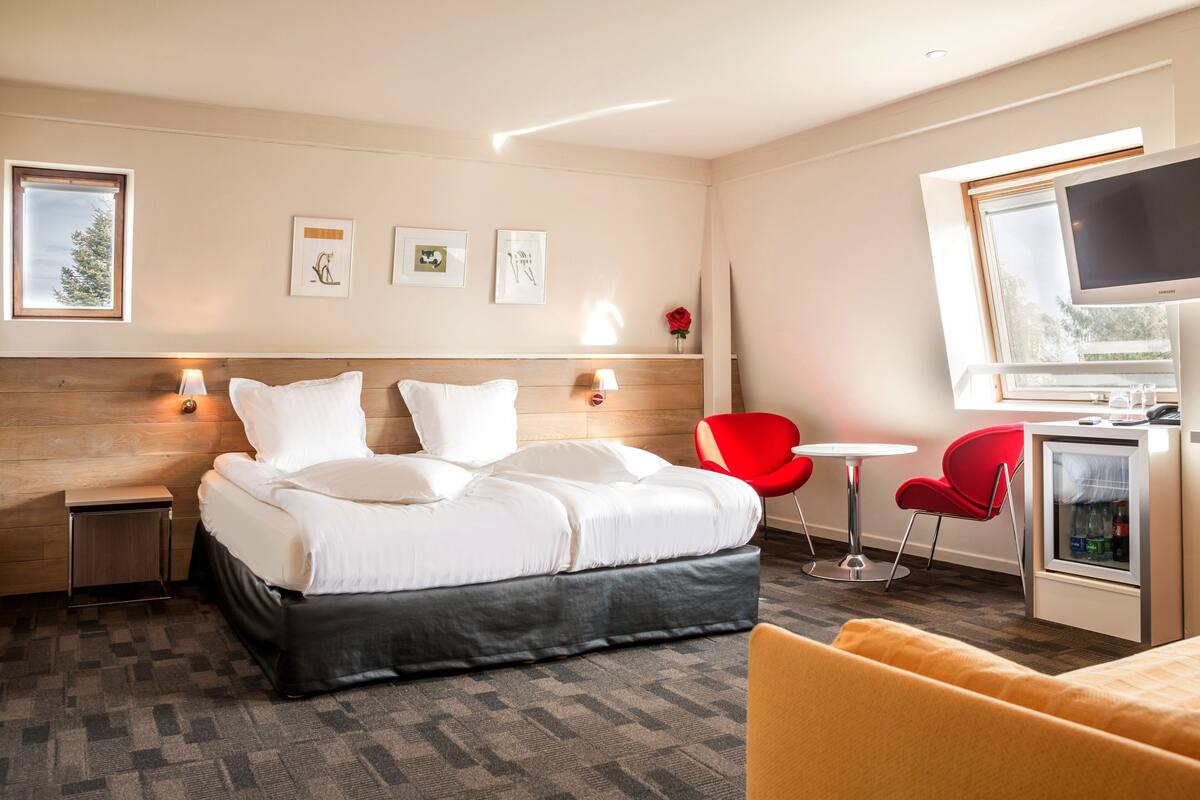 A modern hotel room with a large bed, a desk, a TV, and a red chair.
