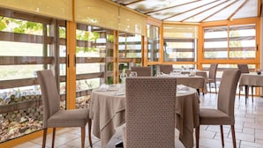 A restaurant with a glass enclosure, wooden flooring, and tables set for dining. - Hotel La Rochette (Labaroche)