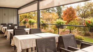 An outdoor dining area with tables and wicker chairs, overlooking a garden with autumn foliage. - Hotel La Rochette (Labaroche)