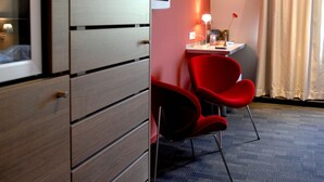 A hotel room with a wooden wardrobe, a desk with a lamp, two red chairs, and a large window with curtains. - Hotel La Rochette (Labaroche)