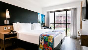 A hotel room with a bed, bedside table, lamp, and a large window with curtains.