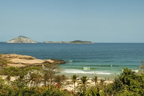 Ein Strand mit klarem Wasser, Felsformationen und in der Ferne Inseln.