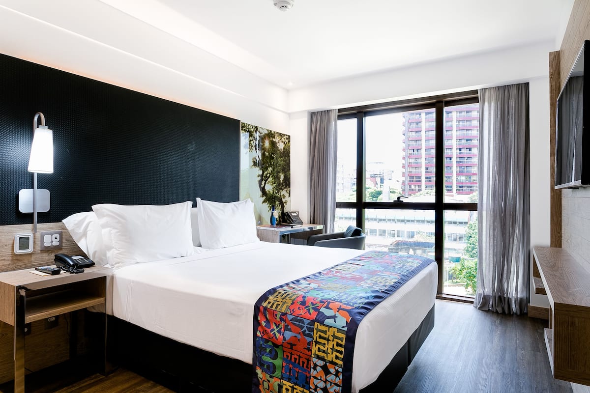 Habitación de hotel con una cama grande, un escritorio con teléfono, televisión y ventana con cortinas.