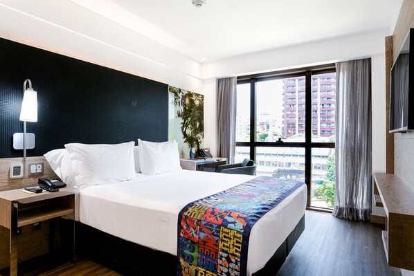 Habitación de hotel con una cama grande, un escritorio con teléfono, televisión y ventana con cortinas.