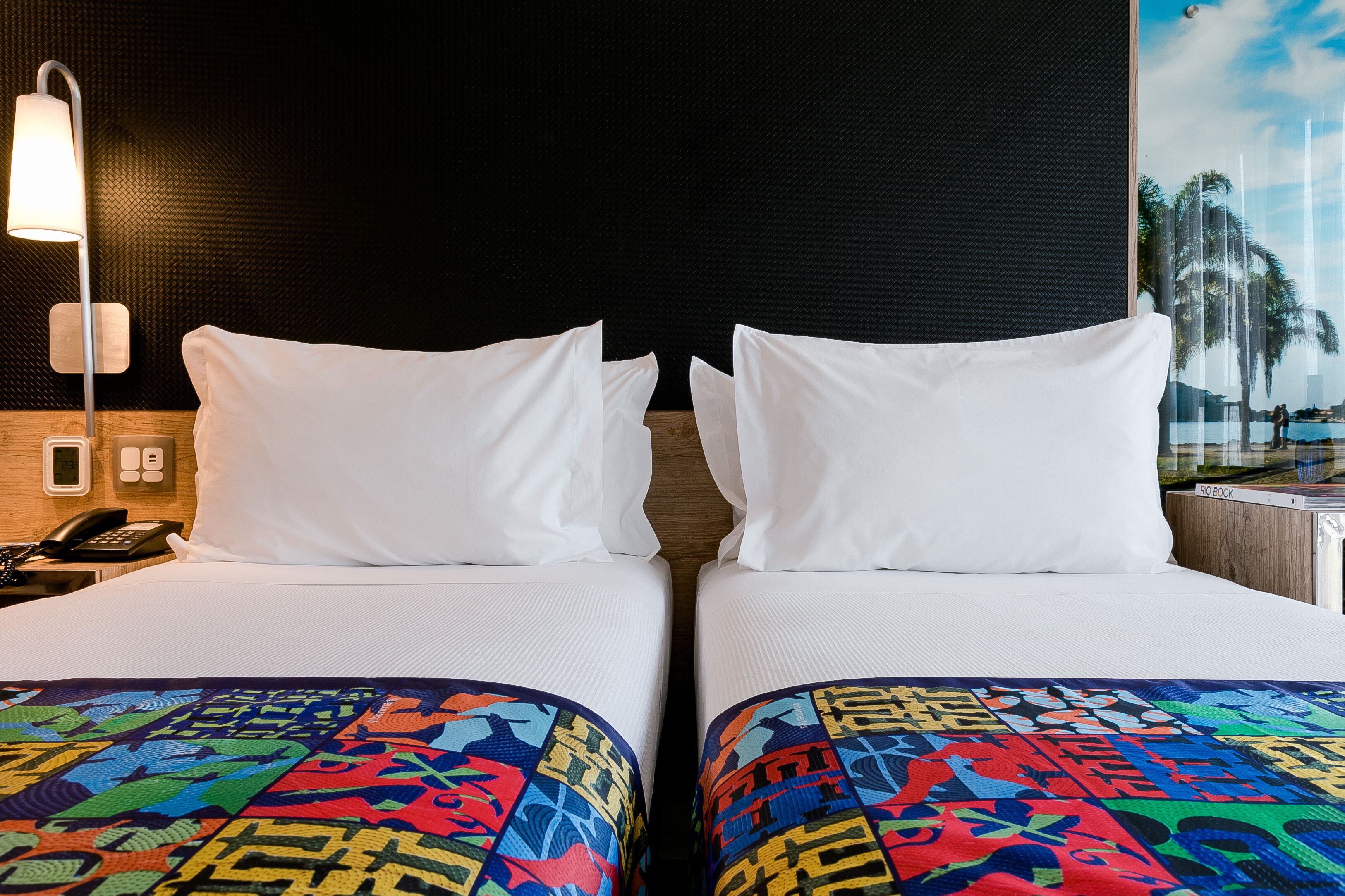 Une chambre d’hôtel avec deux lits, une table de chevet avec un téléphone et une lampe fixée au mur.