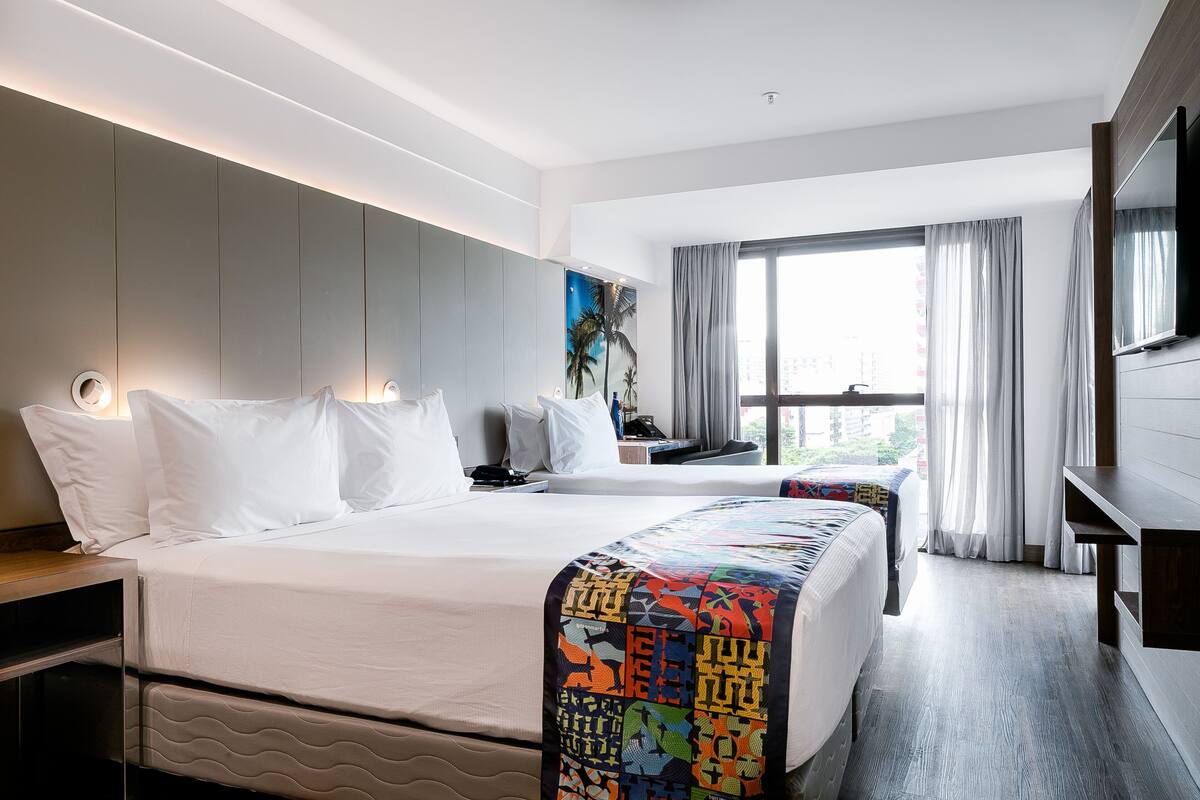 Una habitación de hotel con una cama grande, un escritorio, un televisor y una ventana con cortinas.