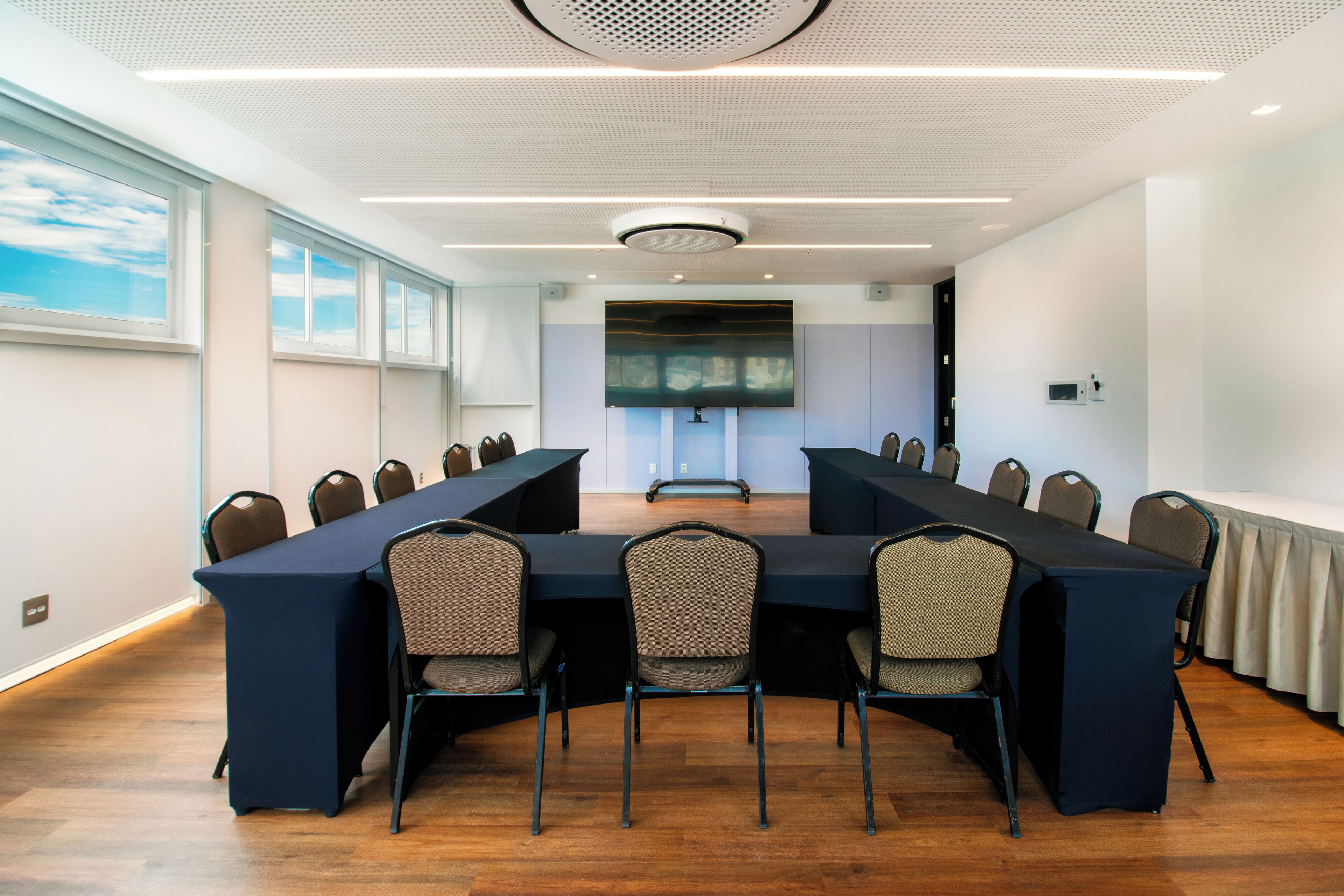 Un salón de conferencias con una larga mesa, sillas, una pantalla de proyector y una lámpara en el techo.