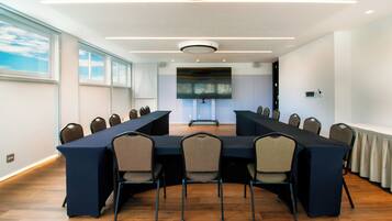 Un salón de conferencias con una larga mesa, sillas, una pantalla de proyector y una lámpara en el techo.