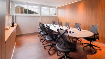 Un salón de conferencias con una larga mesa, sillas de malla negra y una pared de paneles de madera.