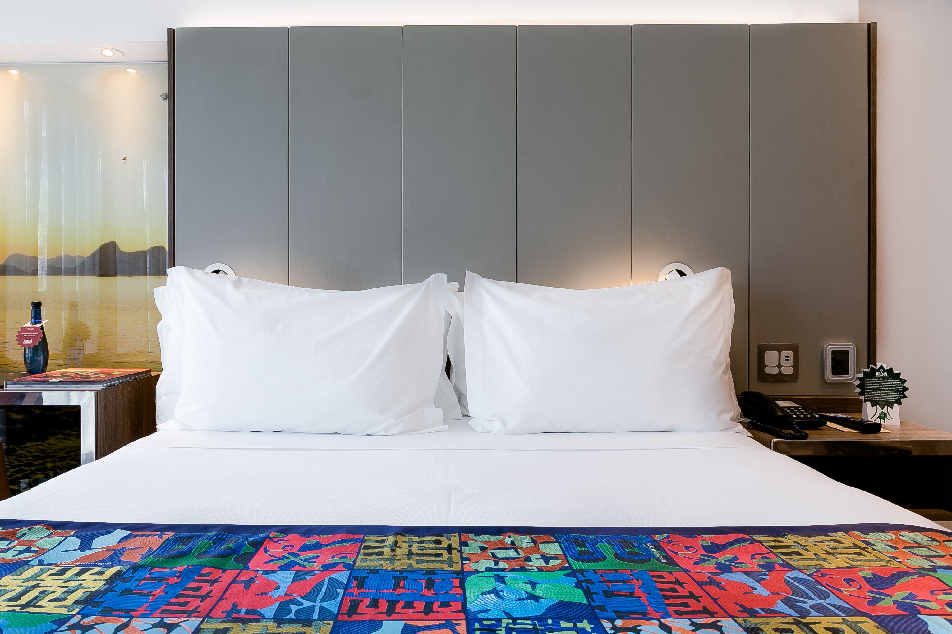 Une chambre d’hôtel avec un lit, une table de chevet, un téléphone et un mur orné d’un tableau.