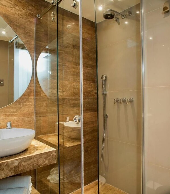 A modern bathroom with a glass shower enclosure, a round mirror, and a marble countertop. - Arena Ipanema Hotel (Rio de Janeiro)