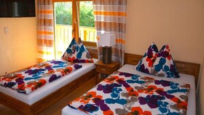 A room with two beds, each with a floral bedspread, a wooden headboard, a bedside table with a lamp, and a window with curtains. - Pension Milan (Zell am See)