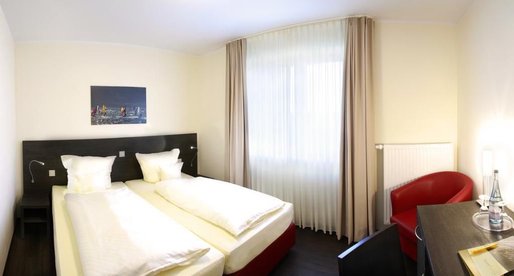 Ein Hotelzimmer mit einem Doppelbett, einem roten Sessel, einem Schreibtisch mit Lampe und einem Bild an der Wand.